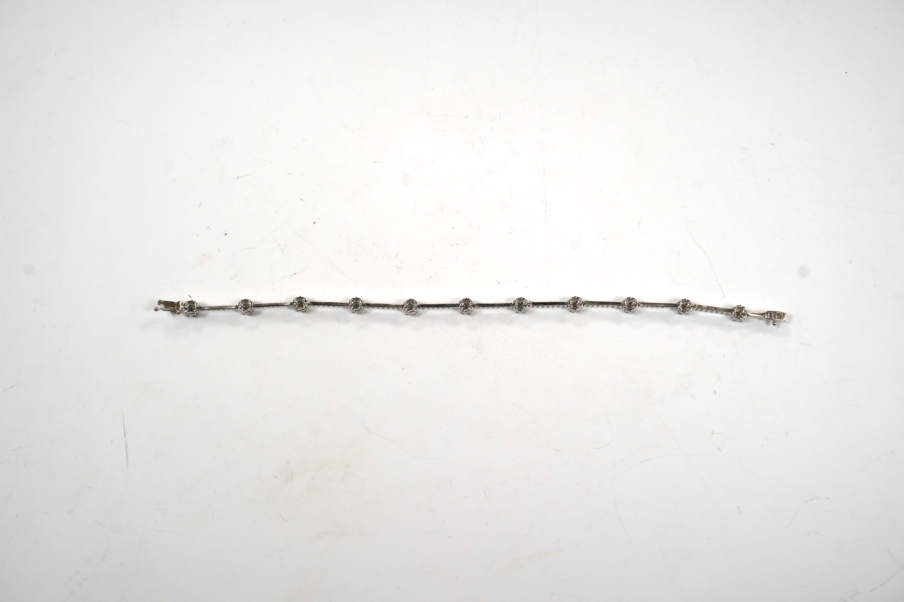 A modern 18k white metal and diamond cluster set line bracelet, 17.8cm, gross weight 8.8 grams.